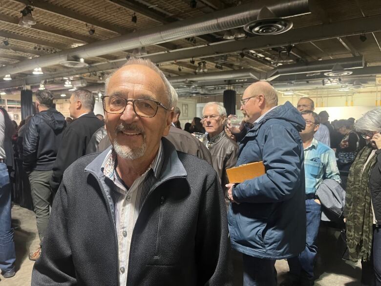 A older man smiles in a crowded convention hall.