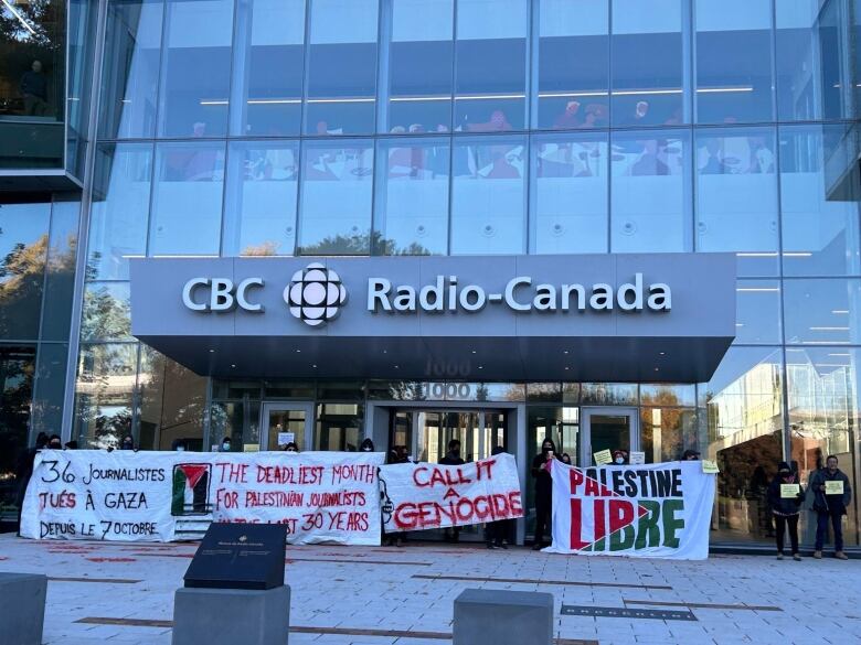 Protesters outside the CBC/Radio-Canada building holding signs that say 