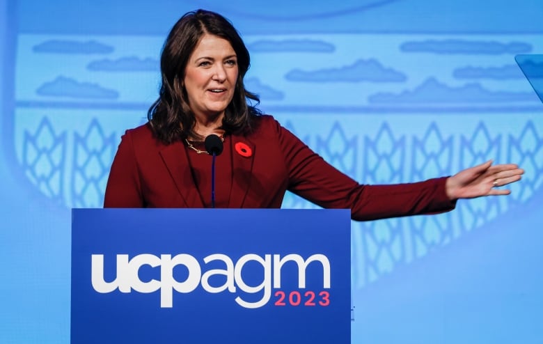 a woman extends her left hand while speaking at a lectern.