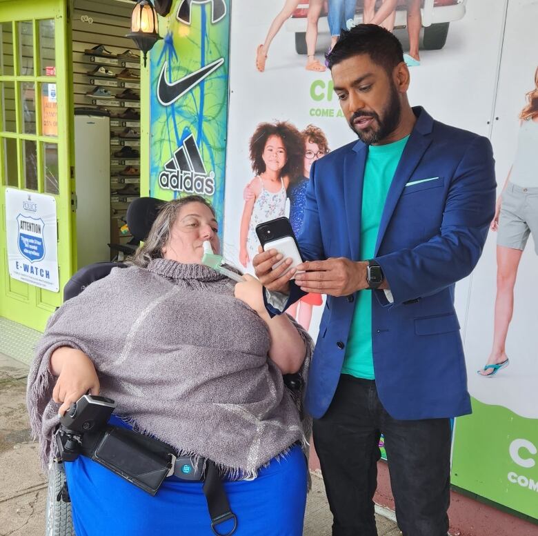 Alessia and Travis are outside in front of a shop looking at Travis' phone.