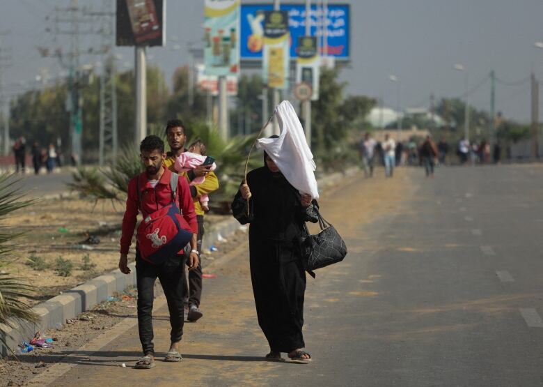 A person holds a white flag as they and a group of people walk on a highway.