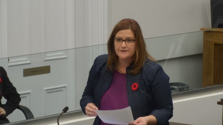 A woman in a striped suit and purple shirt standing posing questions to other politicians.