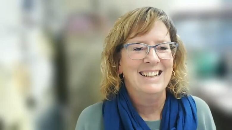 A woman wearing glasses smiles during a Zoom call.