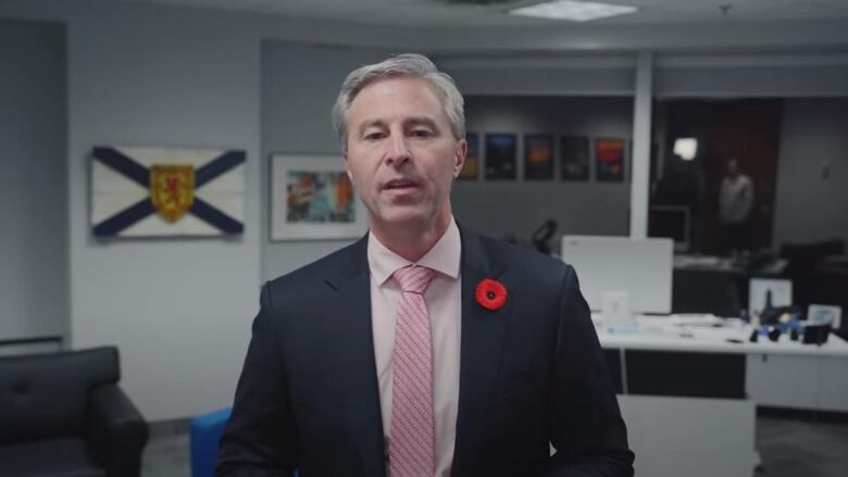 A man wearing a suit stands in an office space.