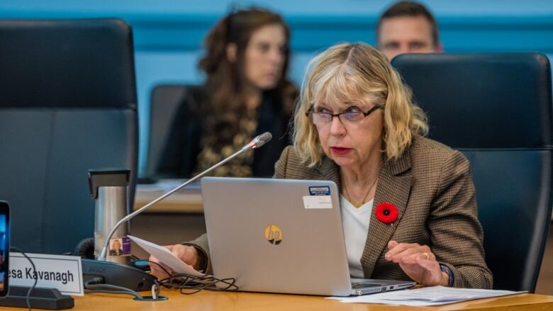 A woman sits behind a microphone at a public meeting.