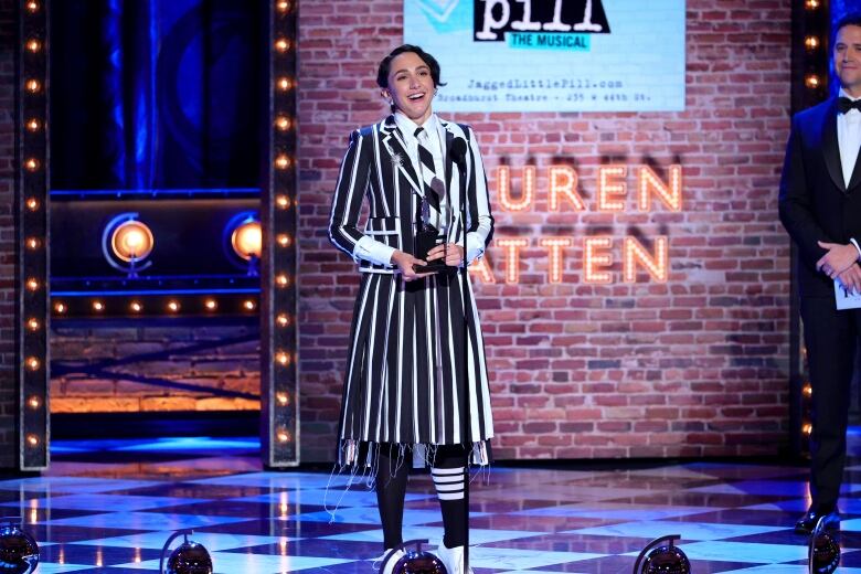 A woman wearing a black and white dress smiles while speaking on a stage. 