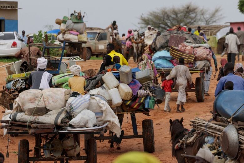 Several carts loaded with bags, jugs and other items on a crowd dirt road.