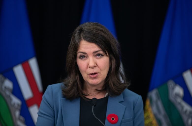 A woman with brown hair in a blue suit stands at a podium. 