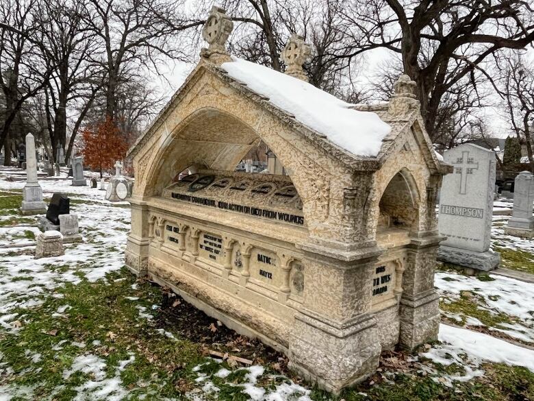 A stone tomb stands in a cemetery with snow on the ground.