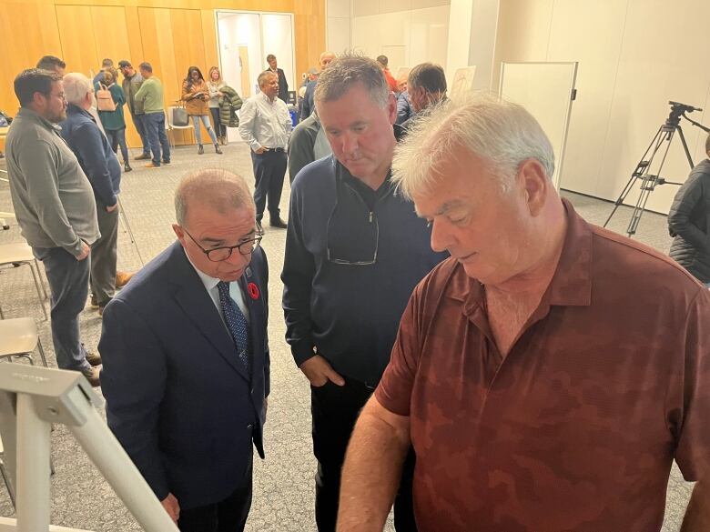 Three men look closely at a chart set up in the middle of the room. 