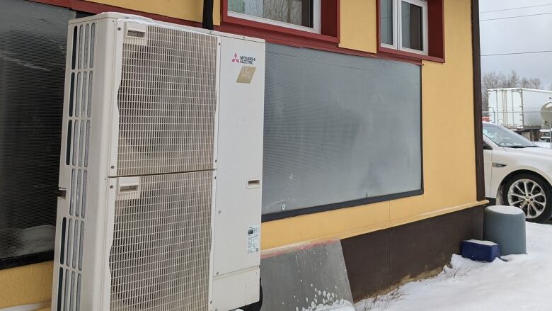 A heat pump is seen on the side of a house in winter.