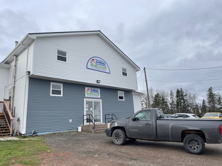 The white and blue building that houses the daycare is shown from the outside, with a truck in the parking lot. 