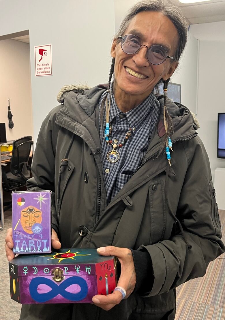 Ron Ewenin-Wapemoose with a colourful box and a deck of cards titled 