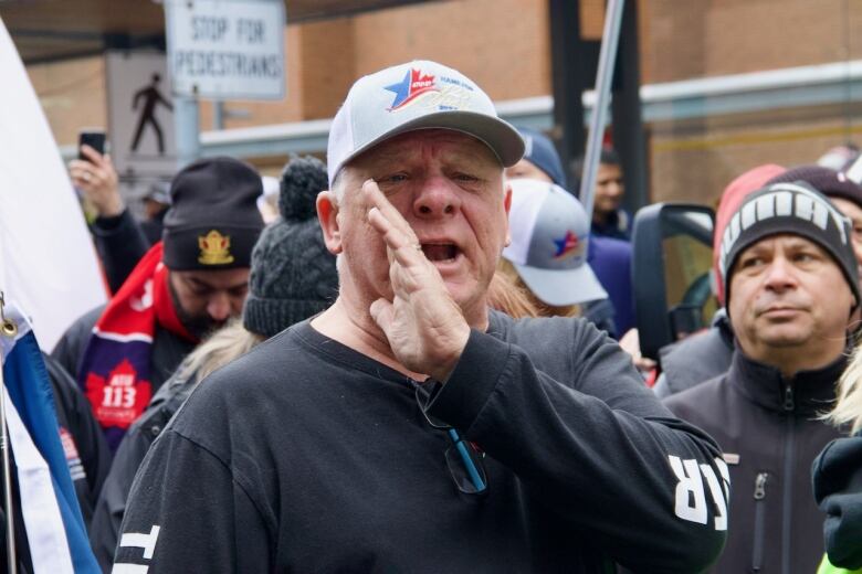 A person in a crowd shouts, holding a hand to his mouth. 