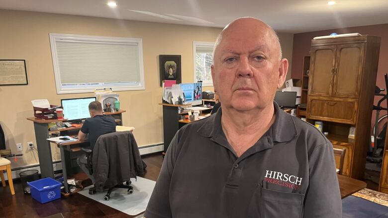 A solemn-looking bald man wearing a dark polo shirt looks into the camera. 