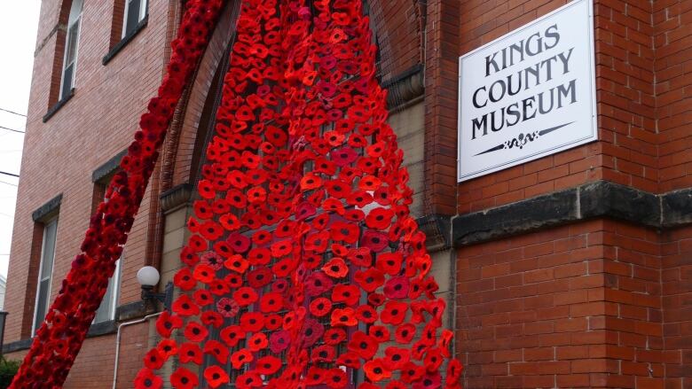 Thousands of poppies hang on a light fabric above the doors of an old brick building. 