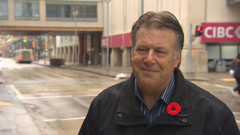 A man in a black jacket, poppy and blue button down is pictured on a downtown Winnipeg street.