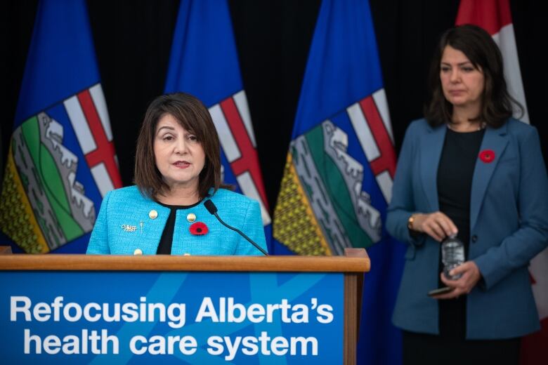 A woman address the media from behind a podium as another woman looks on.