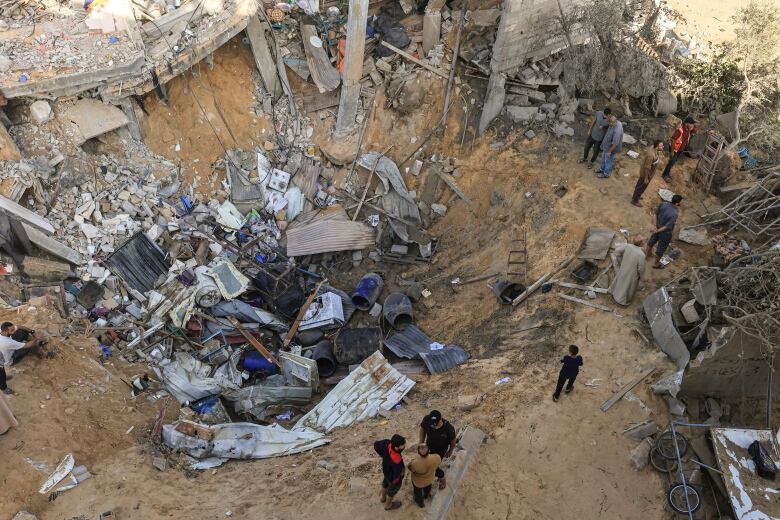 People stand at the edge of a crater filled with debris following an airstrike.