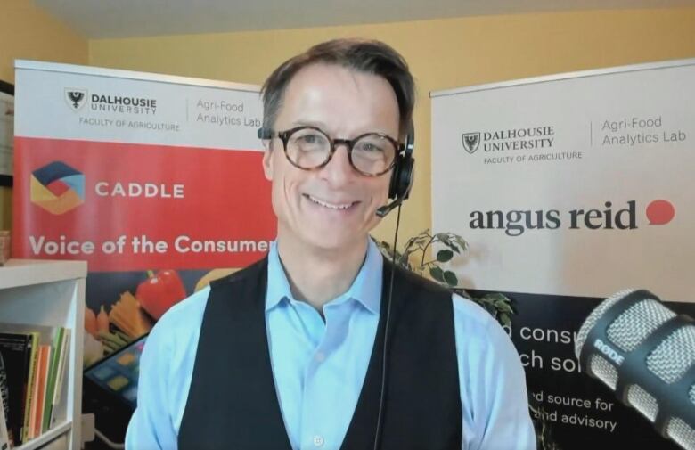 A man in a collared shirt and vest speaks with a headset on