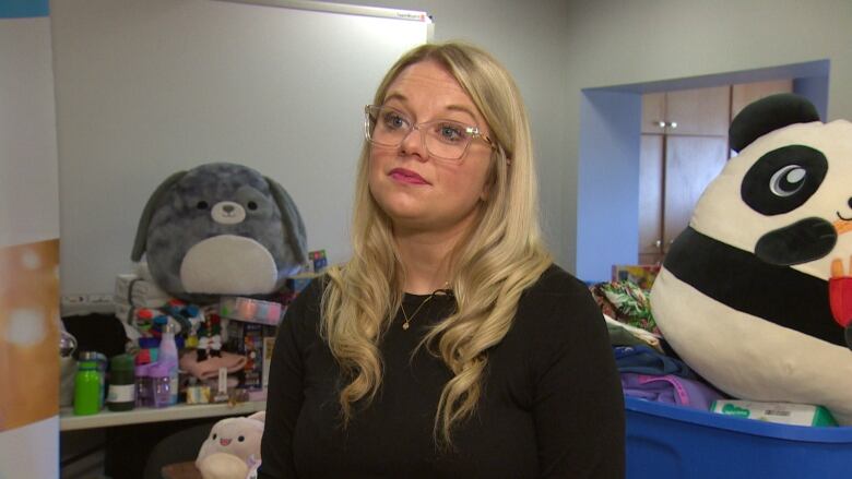 A woman wearing a black shirt and glasses stands in a room filled with toys.