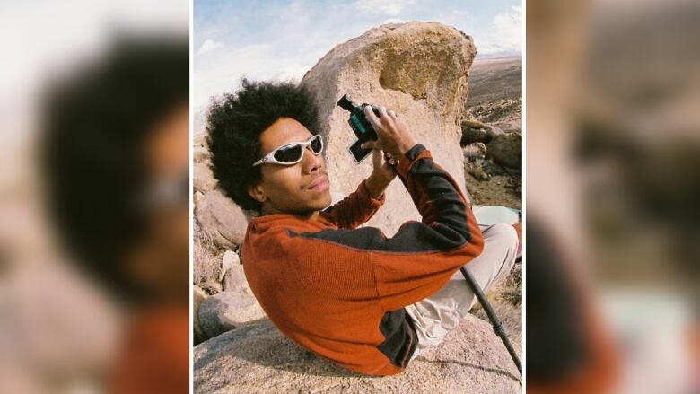 A fish eye view of a man in shades on top of a boulder in a rocky landscape