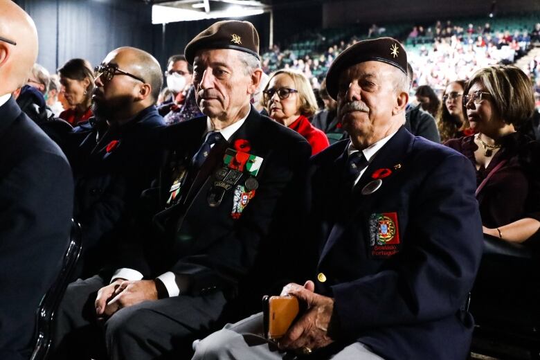 People wearing a uniform and poppies sit in a crowd.