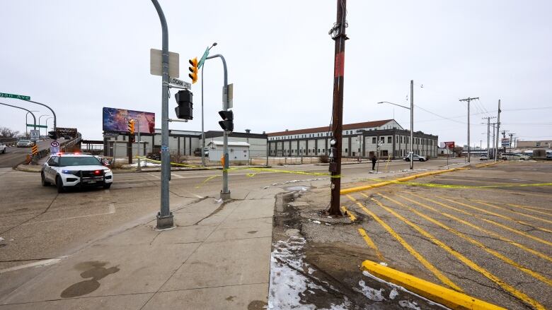 A police car sits next to an intersection beside yellow police tape.