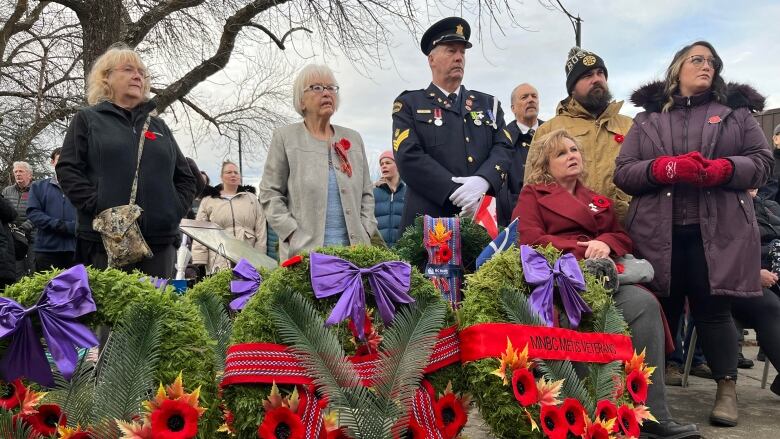 People including a man in military uniform gather wearing red poppies behind wreaths for a memorial ceremony.