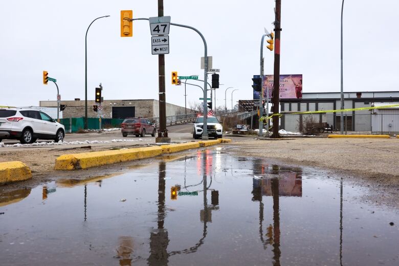 A puddle of water sits in the foreground while a police car sits at an intersection in the background.