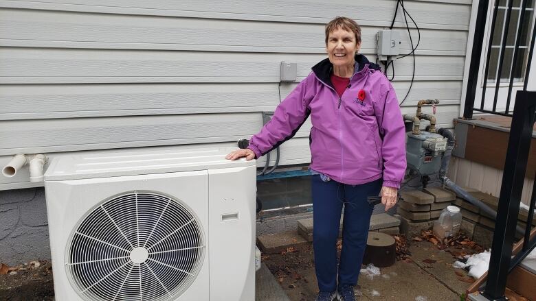 Catherine Gibson stands next to her heat pump behind her Regina home.