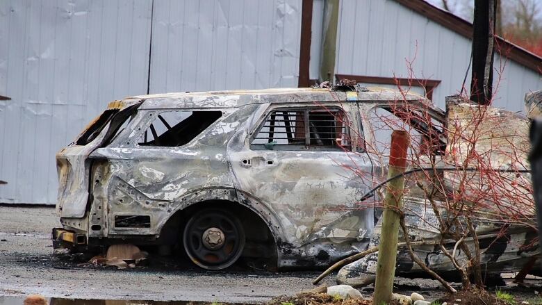 A police vehicle is burned out in front of a buiding.