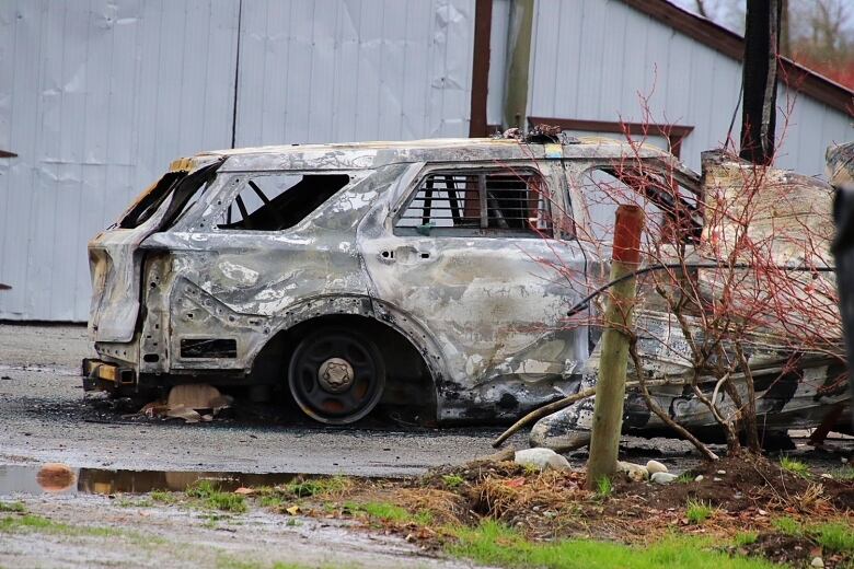 A police vehicle is burned out in front of a buiding.