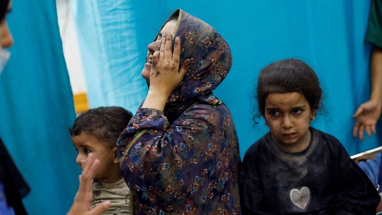 A woman reacts while sitting with two children inside a hospital.