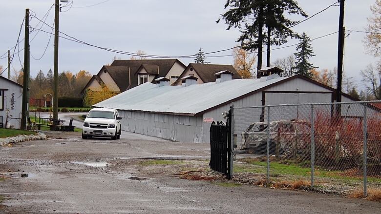 Two police cars sit on a farm property, one of them burned out.