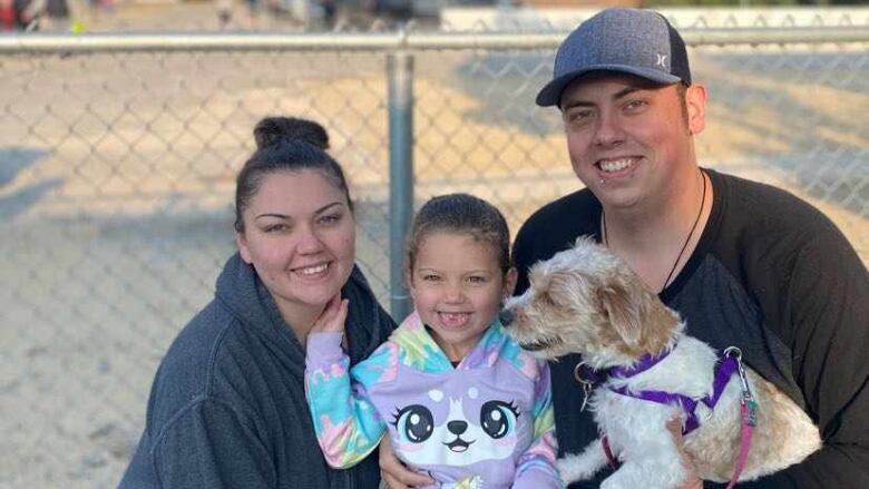 A family of three and their dog kneel for a photo neck to a fence.