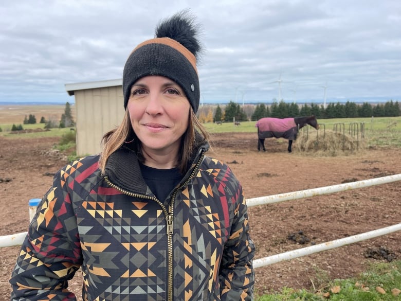 A woman poses for the camera with a horse in the background.