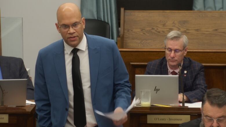 A man in a blue suit and white shirt stands while posing questions to the premier.