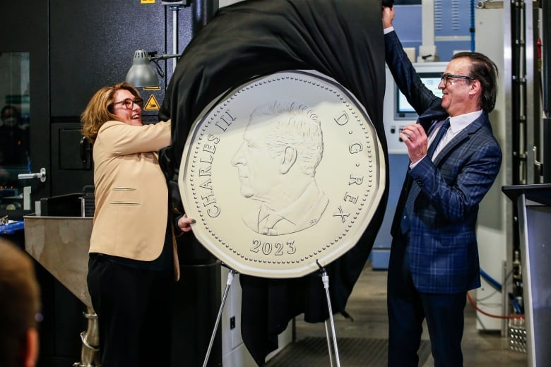 Two people remove a cover from a large replica coin.