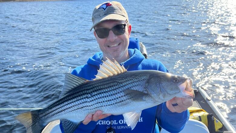 A man in a ball cap and blue sweatshirt smiles while holding a fish.