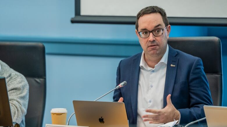 A politician speaks while sitting at a table during a meeting.