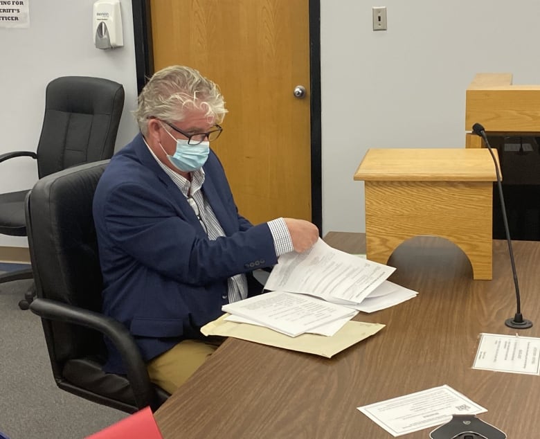 A man wearing a medical mask sits in court with papers in arrayed in front of him.