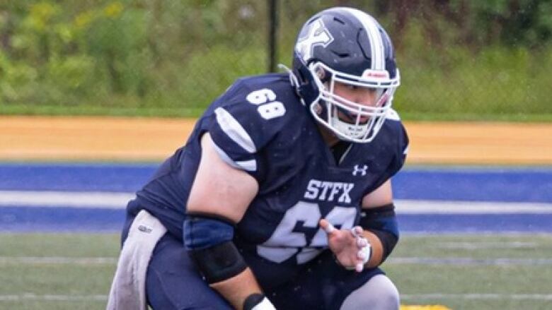 a football player squats and holds the ball close to his body on the field 