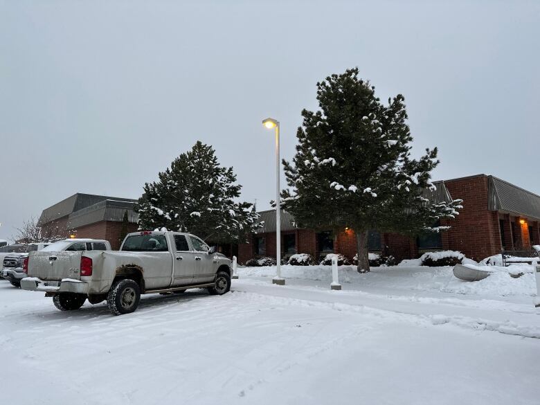 A brick building sits in snow with a white pick up truck parked out front.