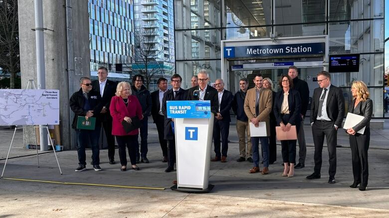 A group of Lower Mainland politicians stand outside the Metrotown SkyTrain staion.