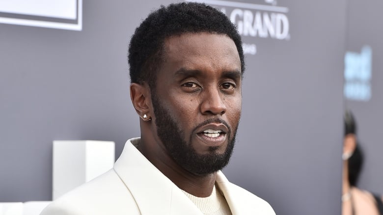 A man in a white suit stands in front of a photowall. 