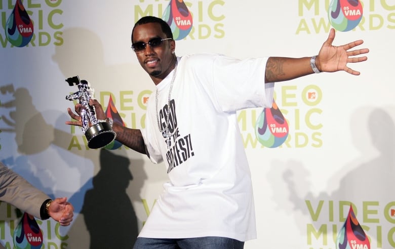 A man poses in front of a photowall. He holds a silver statuette in his hand. 