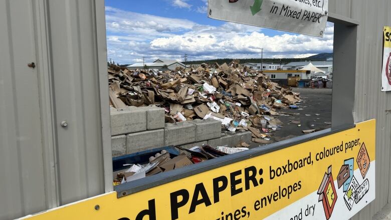 A pile of cardboard is seen through an opening with a sign marked, 'mixed paper.'