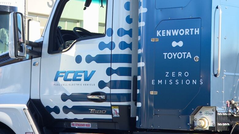 A blue and white transportation truck with fuel cell electric vehicle logos.