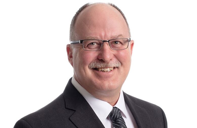 A balding man wearing glasses smiles for a portrait.